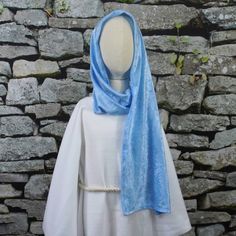 a mannequin wearing a blue shawl in front of a stone wall