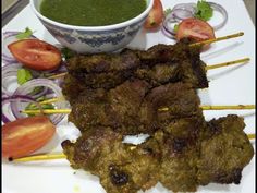 a plate with skewered meat and vegetables next to a bowl of pesto sauce