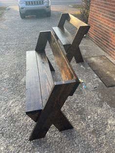 a wooden bench sitting on the side of a road next to a brick wall and parked car