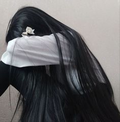 a woman with long black hair is wearing a white shirt and has a flower in her hair