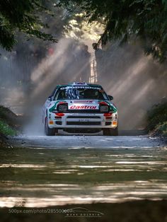 a rally car driving down a dirt road in the sun with dust coming from behind it