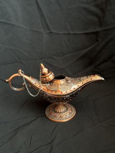 an ornately decorated teapot sits on a black cloth covered table with a chain hanging from the handle