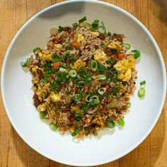 a white bowl filled with rice and veggies on top of a wooden table