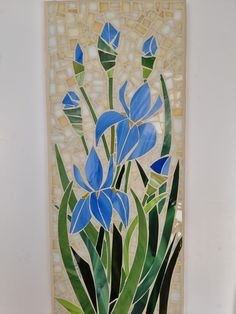 a painting with blue flowers and green leaves on the bottom half of it, in front of a white wall