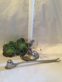 a white candle and some silver spoons on a table with succulents