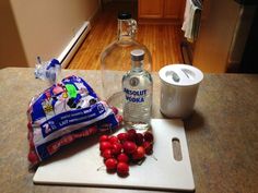 some cherries are sitting on a cutting board next to a bottle of vodka and a bag of chips