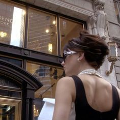 a woman is walking down the street in front of a building wearing sunglasses and carrying shopping bags