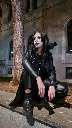 a woman sitting on the ground in front of a tree with her face painted white