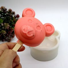 a pink bear popsicle sitting on top of a white cup next to a plant