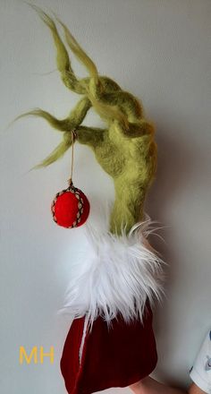 a hand holding a red and white christmas stocking ornament with green hair