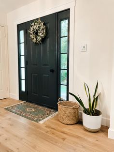 a black front door with a wreath and potted plant on the floor next to it