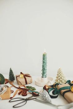 a white table topped with lots of different types of christmas decorations and presents next to a lit candle