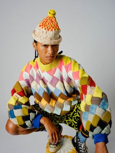 a young man is sitting on top of a skateboard wearing a colorful sweater and hat