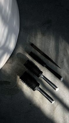 three black brushes sitting next to each other on top of a white bowl and floor