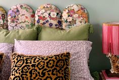 a bed topped with lots of pillows next to a pink lamp and a green wall