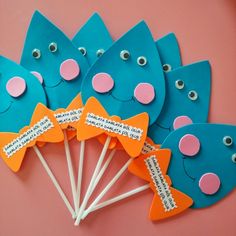 blue and orange fish shaped lollipops with words on them sitting on a pink surface