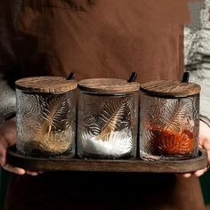 a person holding a tray with four jars filled with spices and seasoning on it