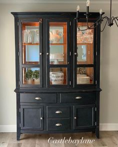 a black china cabinet with glass doors on the top and bottom, in front of a chandelier