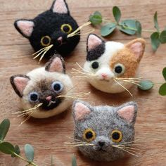 four small felted cats sitting on top of a wooden table next to plants and leaves