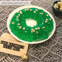 a green frosted doughnut sitting on top of a white plate next to a bowl of gold candies