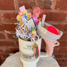 a cup filled with lots of assorted items on top of a white table next to a brick wall