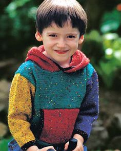 a young boy wearing a multicolored sweater and holding a black object in his hands