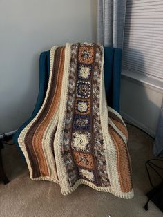 a crocheted blanket sitting on top of a blue chair next to a window