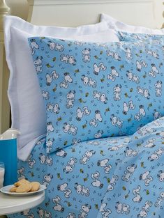 a blue bed topped with lots of pillows next to a tray of cookies and milk