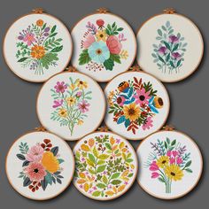 six embroidered floral designs are displayed on wooden hoops, each decorated with different colored flowers