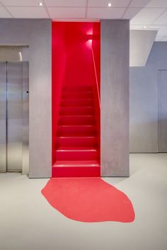 an empty room with red carpet and stairs leading up to the top floor, in front of two stainless steel elevators