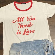 All You Need Is Love Graphic Tee Casual Valentine's Day Tops With Letter Print, Casual Valentine's Day Top With Text Print, Casual Tops With Letter Print For Valentine's Day, Casual Letter Print Tops For Valentine's Day, White Casual Top For Valentine's Day, Casual White Top For Valentine's Day, White Valentine's Day T-shirt With Text Print, Red Retro Slogan Tops, Retro White T-shirt With Heart Graphic