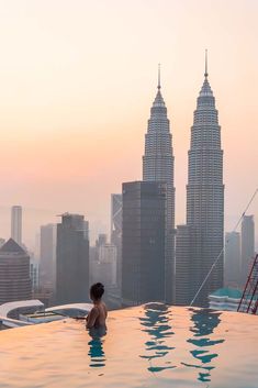 a woman standing in the middle of a swimming pool with two tall buildings in the background