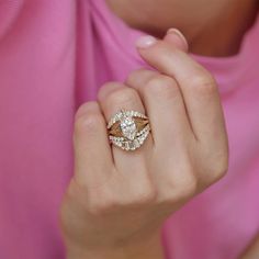 a woman wearing a pink shirt holding a gold and diamond ring