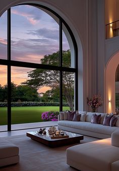 a living room filled with furniture and large windows overlooking a lush green field at sunset