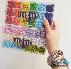 a person holding up a plastic container filled with candy beans and m & m's