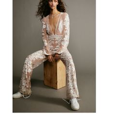 a woman sitting on top of a wooden block wearing white pants and a sheer shirt