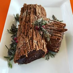 two pieces of chocolate log on a white plate with sprigs and berries around it