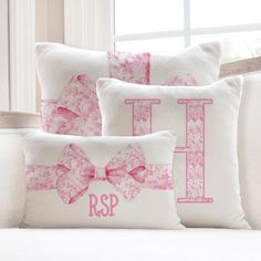 three pillows with pink bows and monogrammed letters are sitting on a white couch