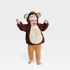 a baby wearing a monkey costume standing in front of a white background with his hands up