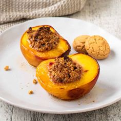 three baked peaches on a white plate next to a cookie