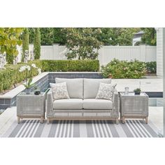 an outdoor patio furniture set in front of a swimming pool and garden area with white striped rugs