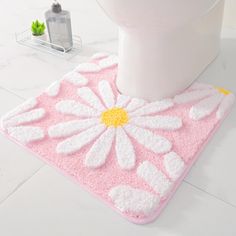 a pink and white bathroom rug with a flower design on the floor next to a toilet