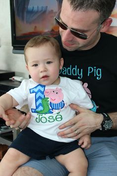 a man holding a baby in his lap while he is wearing a shirt that says daddy pig