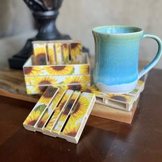 a coffee cup and coasters sitting on a wooden table next to a vase with flowers