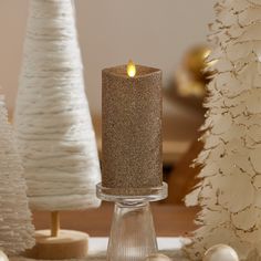 a lit candle sitting on top of a table next to white christmas trees and ornaments