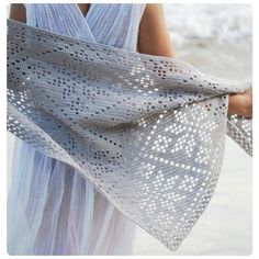 a woman in a white dress holding a shawl on the beach