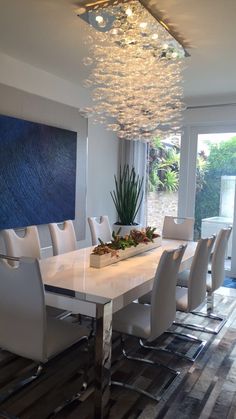 a dining room table with white chairs and a chandelier hanging from the ceiling