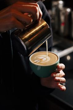 a person pouring coffee into a green cup