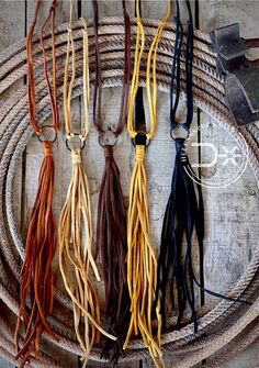 four different colors of leather tassels are on a rope with an old tool in the background