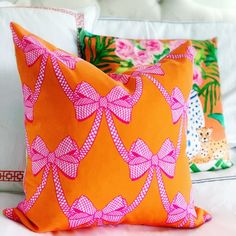 two orange and pink pillows sitting on top of a white couch next to each other